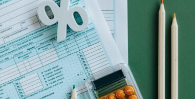 Flat lay of tax documents, calculator, and pencils on green surface.